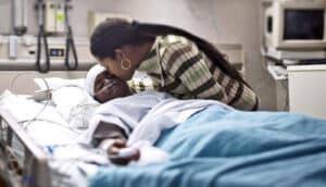 adult leans to kiss child in hospital bed
