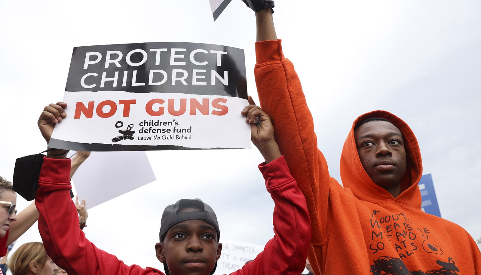 Zwei ernsthafte junge Männer halten ein Protestschild hoch – „Schützt Kinder, nicht Waffen