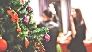 A Christmas tree covered in ornaments with people at a party in the background.