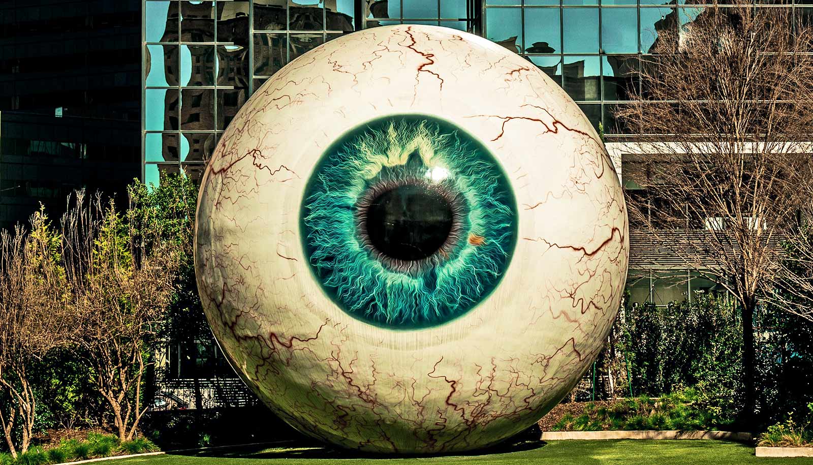 A large eyeball art installation in a park in front of an office building.