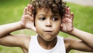 child looks aside while holding hands up by ears