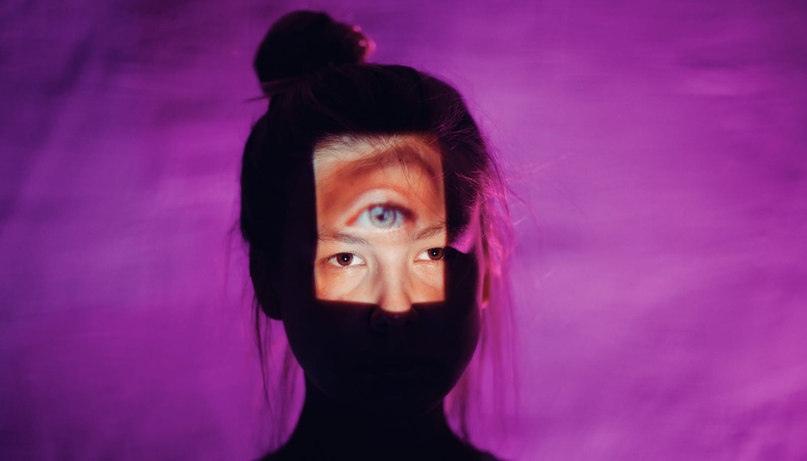 silhouette of face against purple. Rectangle of light on face shows two eyes plus another on the forehead