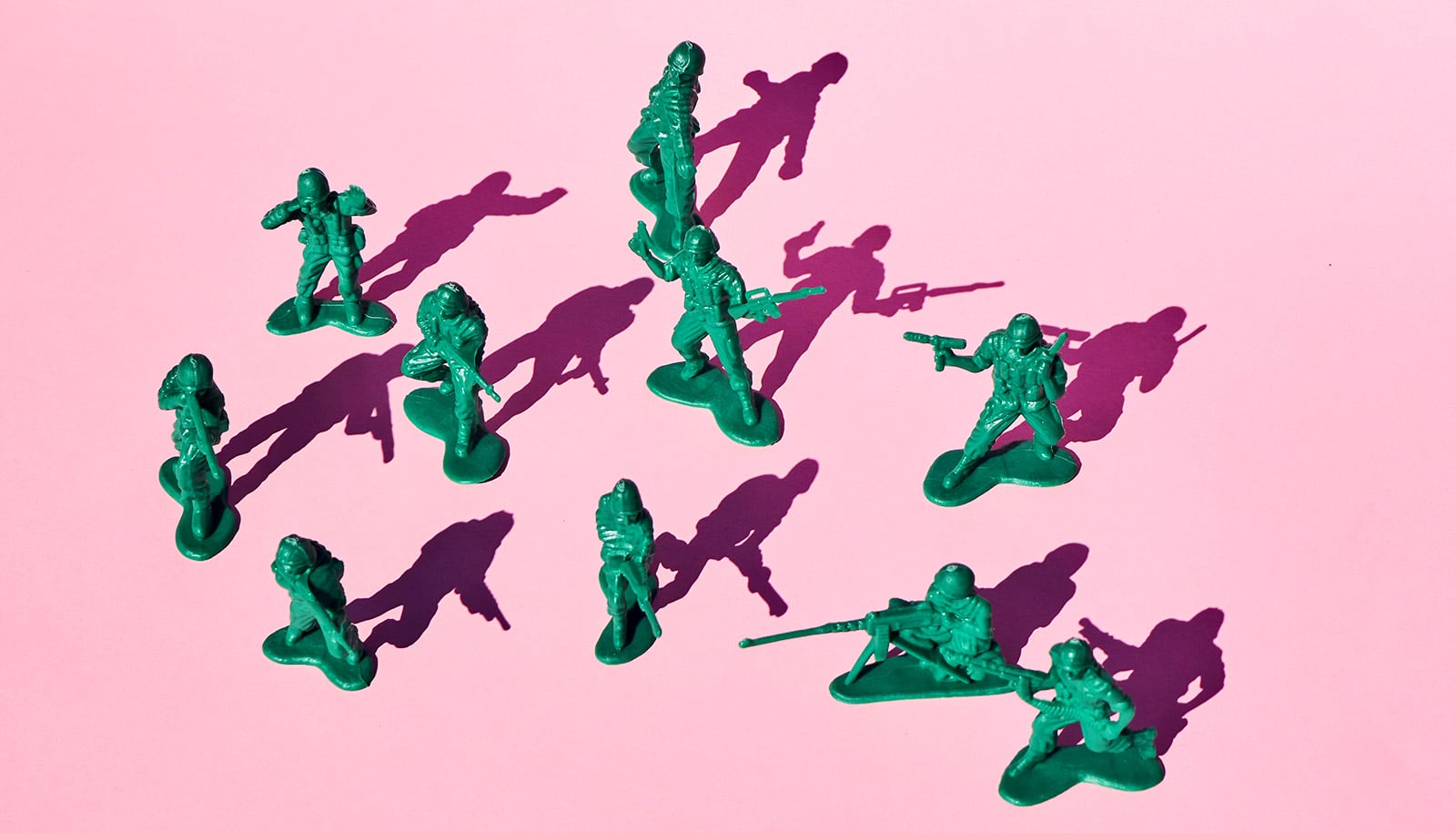 Green army men toys on a pink background.