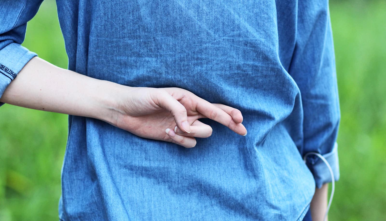 A woman in a blue shirt crosses her fingers behind her back.