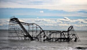 A rollercoaster sticks out of the Atlantic Ocean, with cloudy blue skies in the distance.