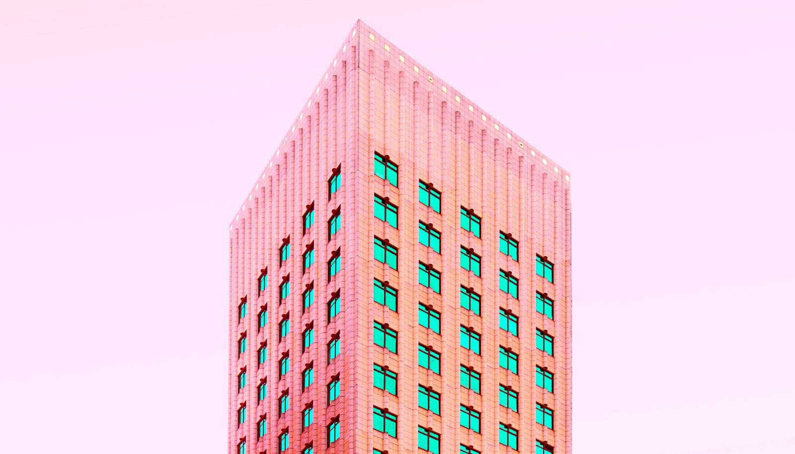 toppen af ​​lyserød bygning med grønne vinduer mod lyserød himmel