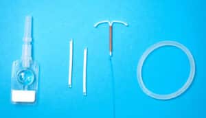 contraceptive devices on blue background: depo, arm implants, IUD, vaginal ring)