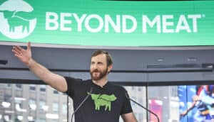 man stands at podium with arm outstretched under "Beyond Meat" sign