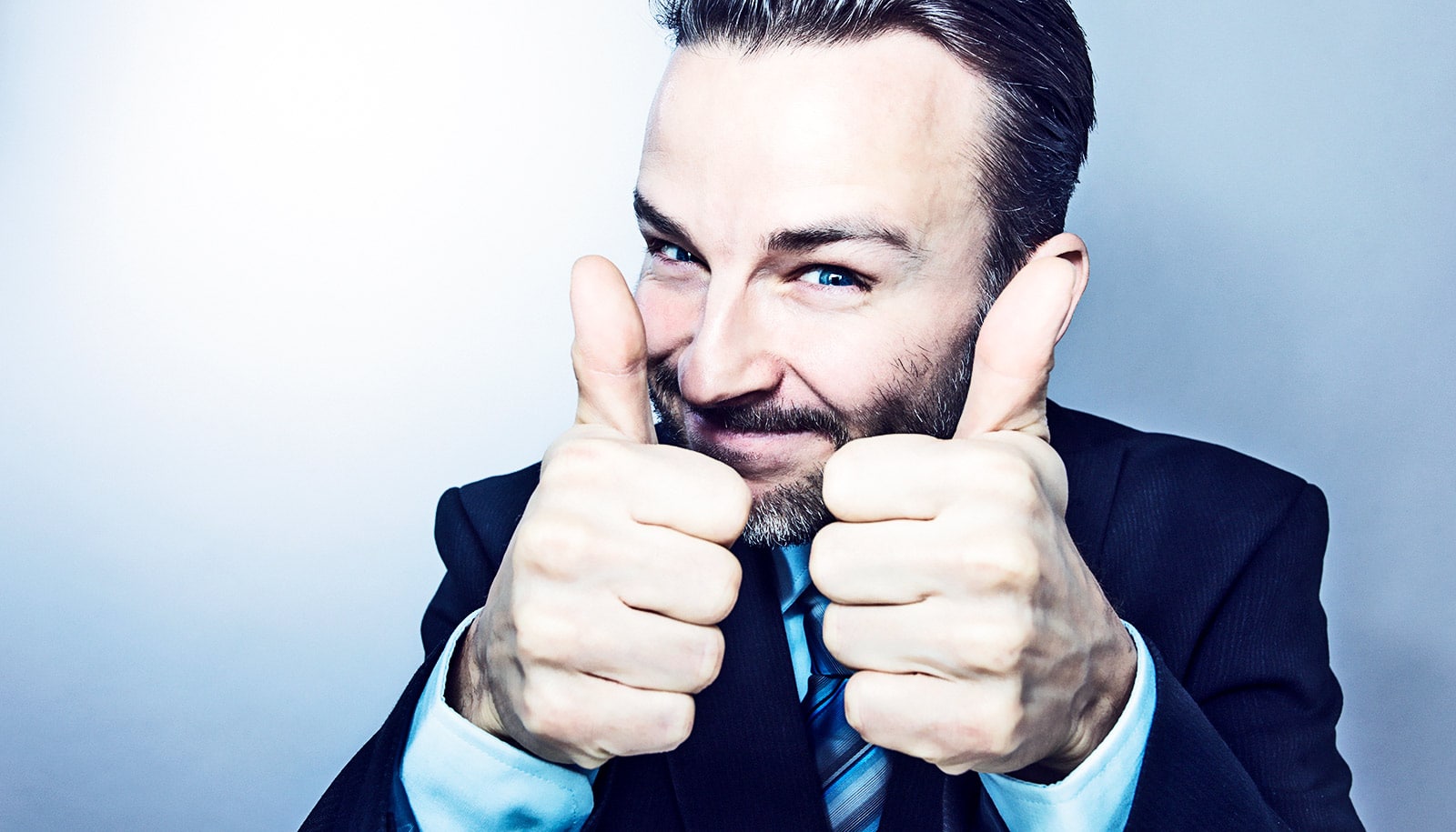 A businessman in a suit gives a double thumbs up and smiles at the camera.