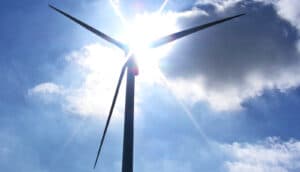 A wind turbine with the sun and blue sky behind it.