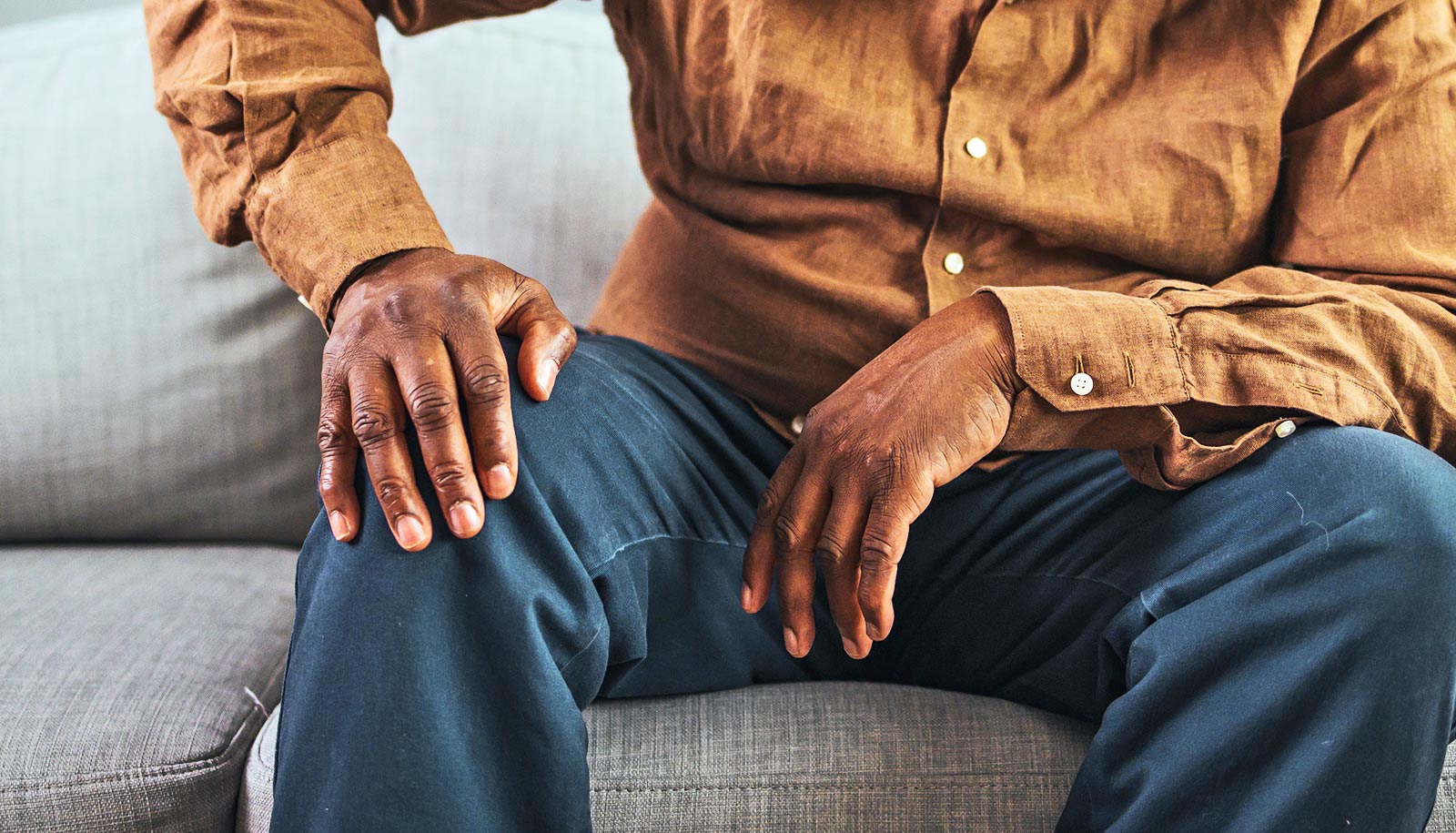 An older man sitting on a couch holds his knee with one hand.