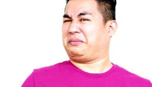 A man in a pink t-shirt has a disgusted look on his face.