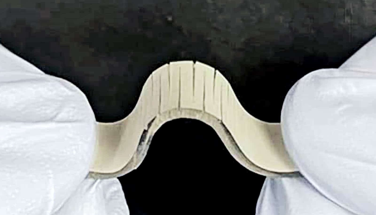 A researcher wearing white gloves bends the flexible sensor so it looks like a bell curve.