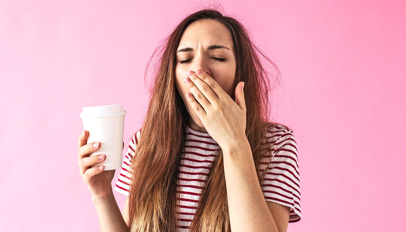 En kvinde, der holder en kop kaffe, gaber, mens hun dækker munden.
