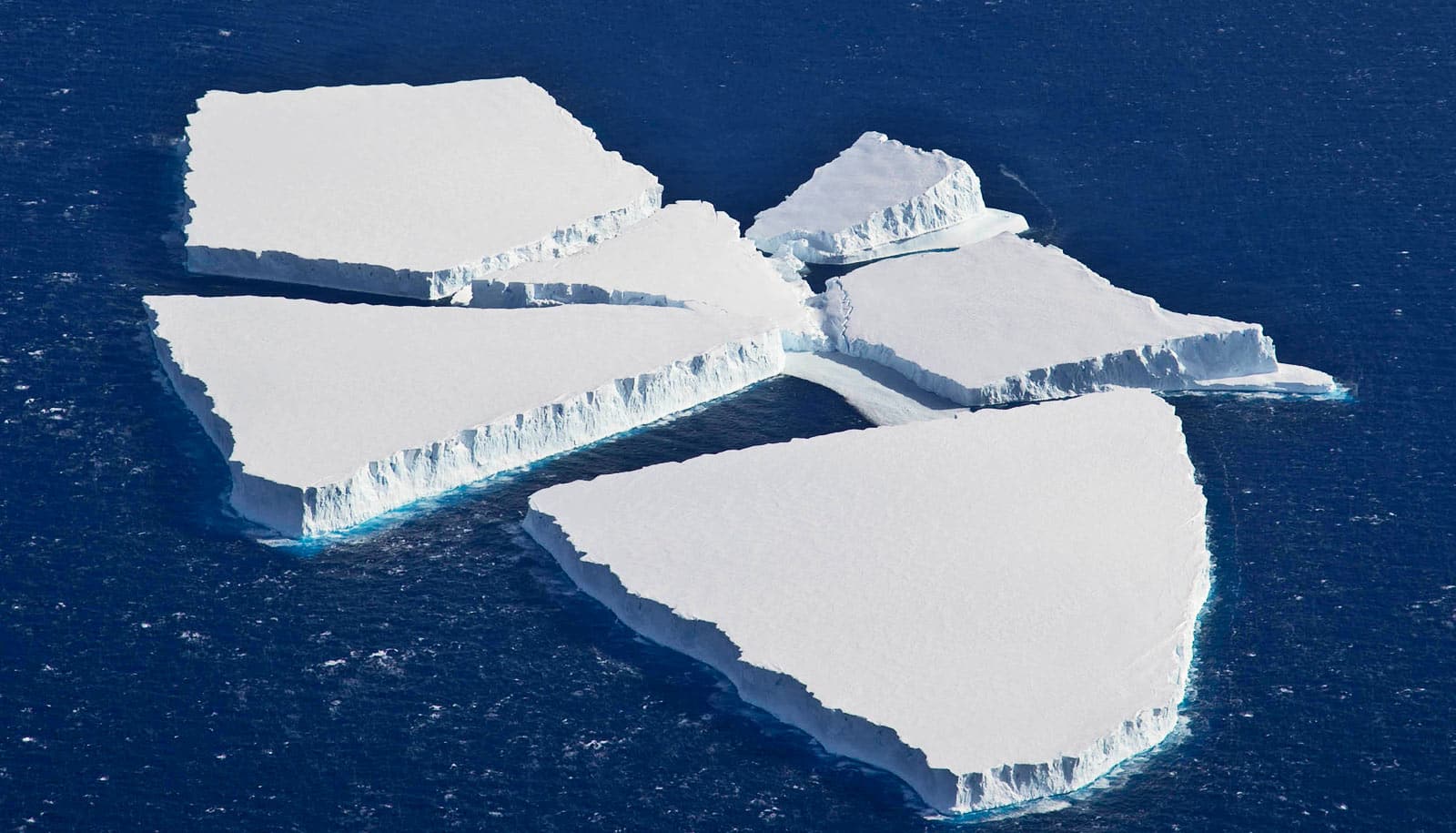 Gezackte weiße Eisberge sitzen nebeneinander im tiefblauen Wasser.