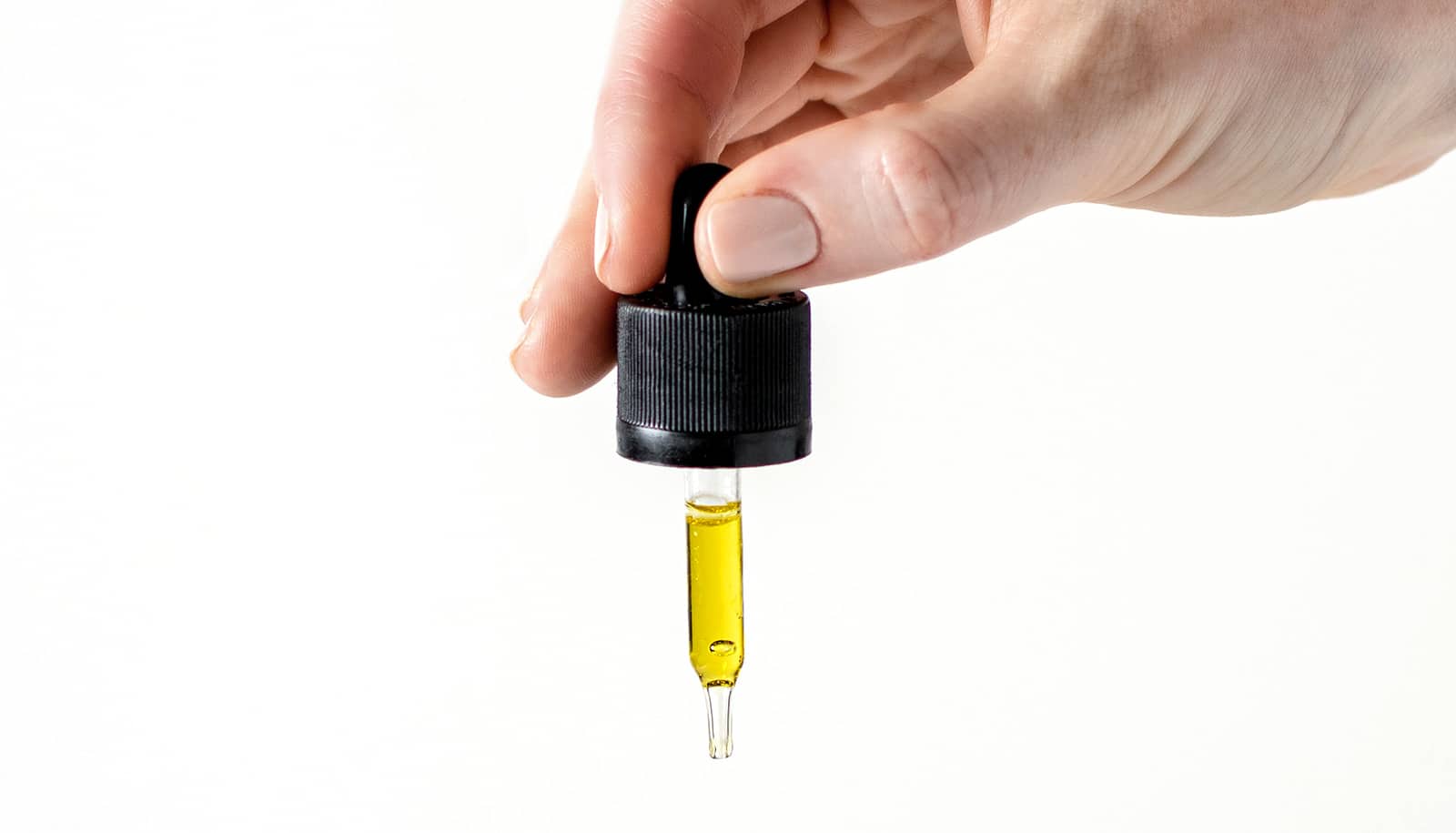 A person uses a dropper with CBD oil in it against a white background.