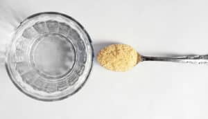 psyllium husk fiber in spoon next to glass of water