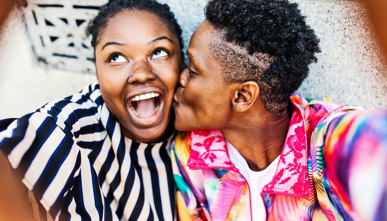 A woman kisses her girlfriend on the cheek while they take a selfie.
