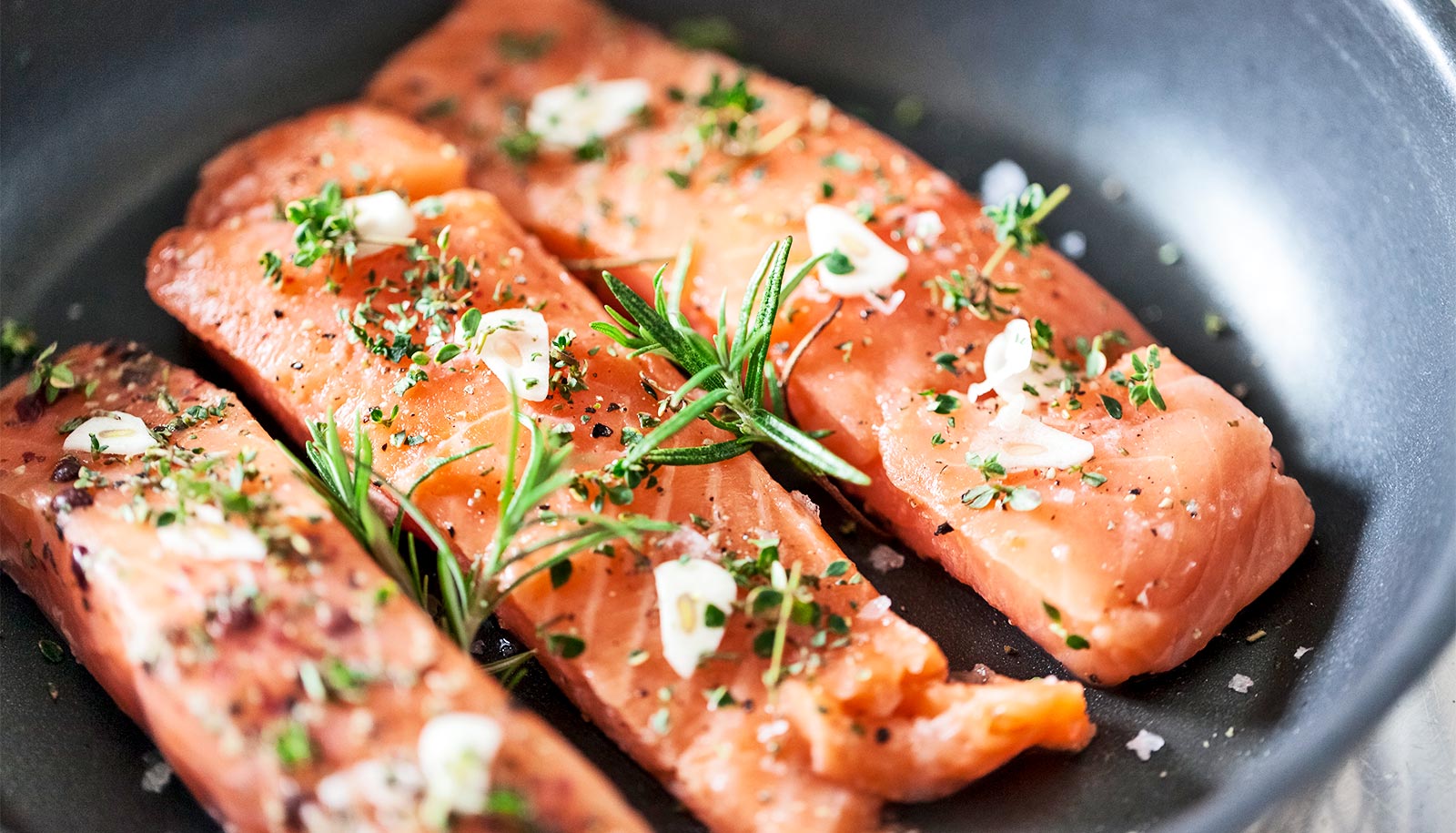 Three pieces of pink salmon cooking in a pan.