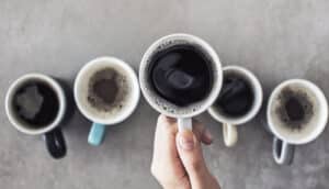 hand holds one mug of coffee above four others