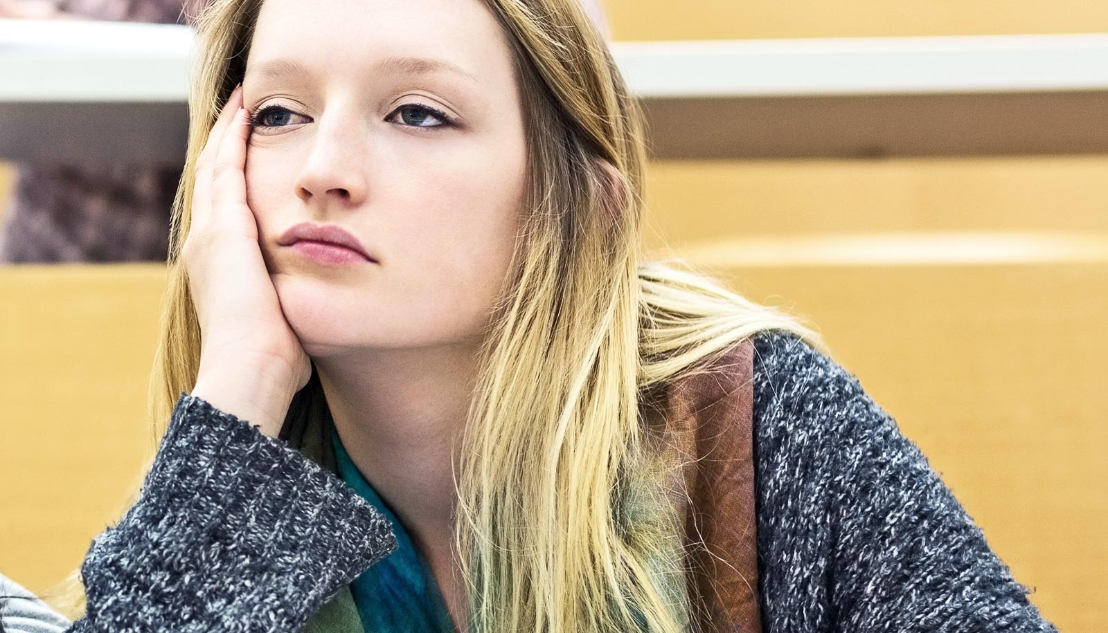 A college student in a lecture class leans on her hand and looks tired.