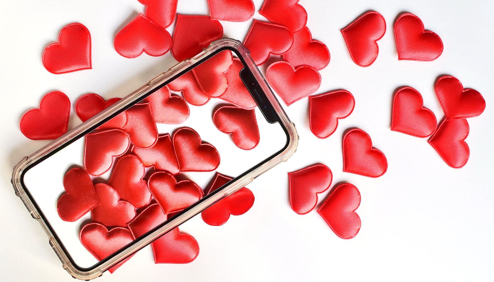 A smartphone with hearts on the screen on top of the same kind of hearts on a white background.