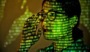 A young woman has binary code projected on her face in green.