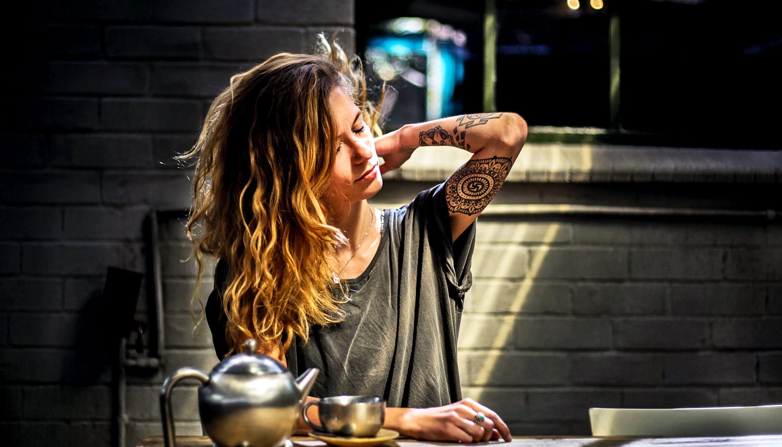 A woman reaches up to her neck while sitting at a kitchen table.
