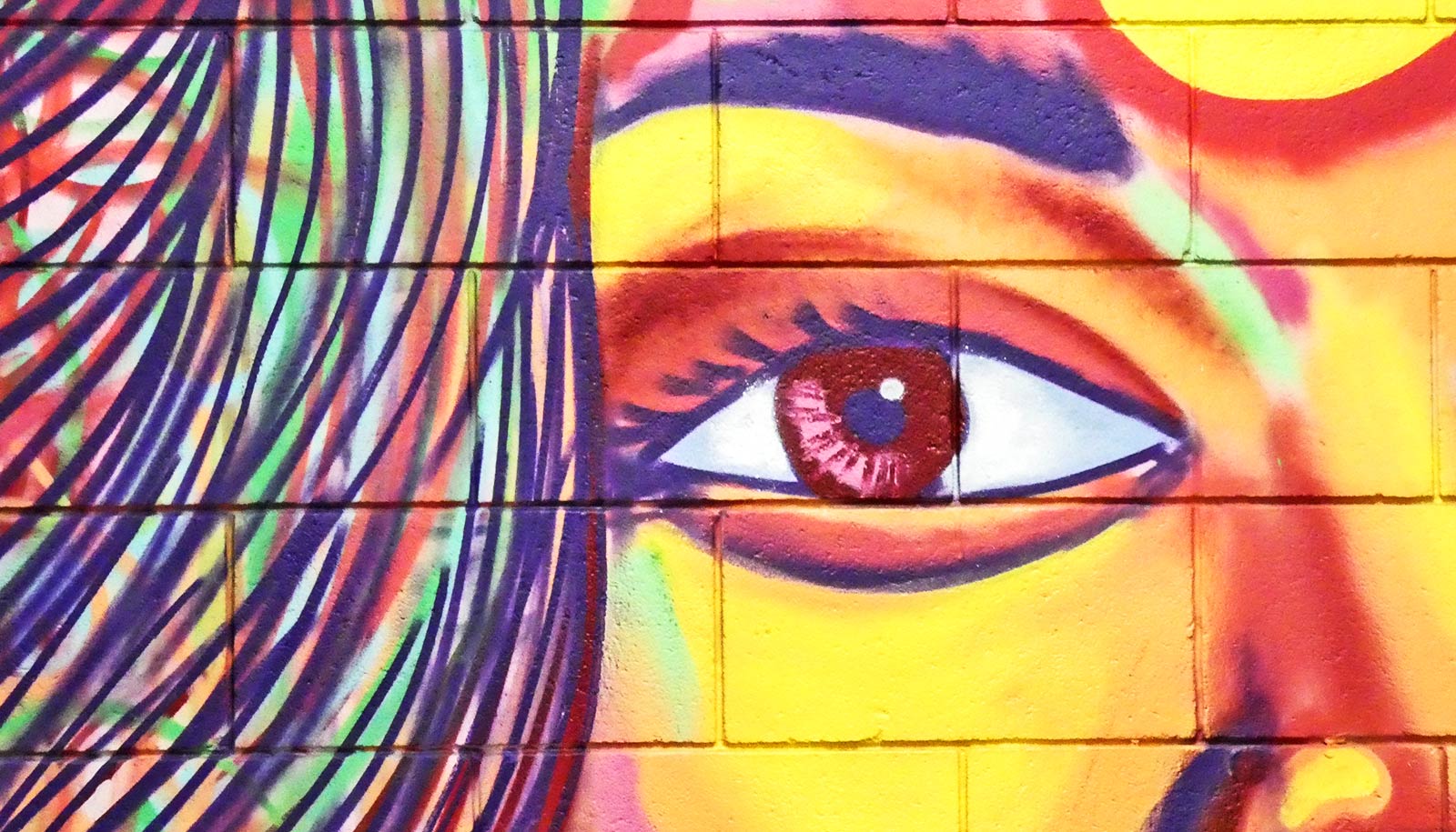 A painted mural shows a woman's eye and hair in bright colors on a brick wall.