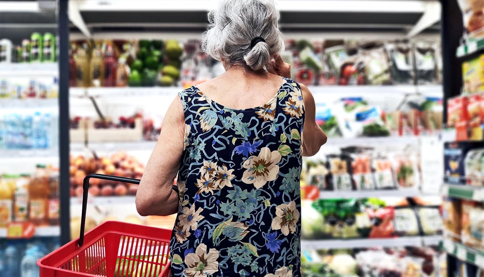 An older woman at the grocery looking at full shelves.