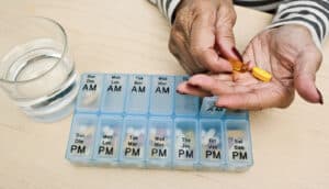 hands hold pills next to pill sorter and glass of water