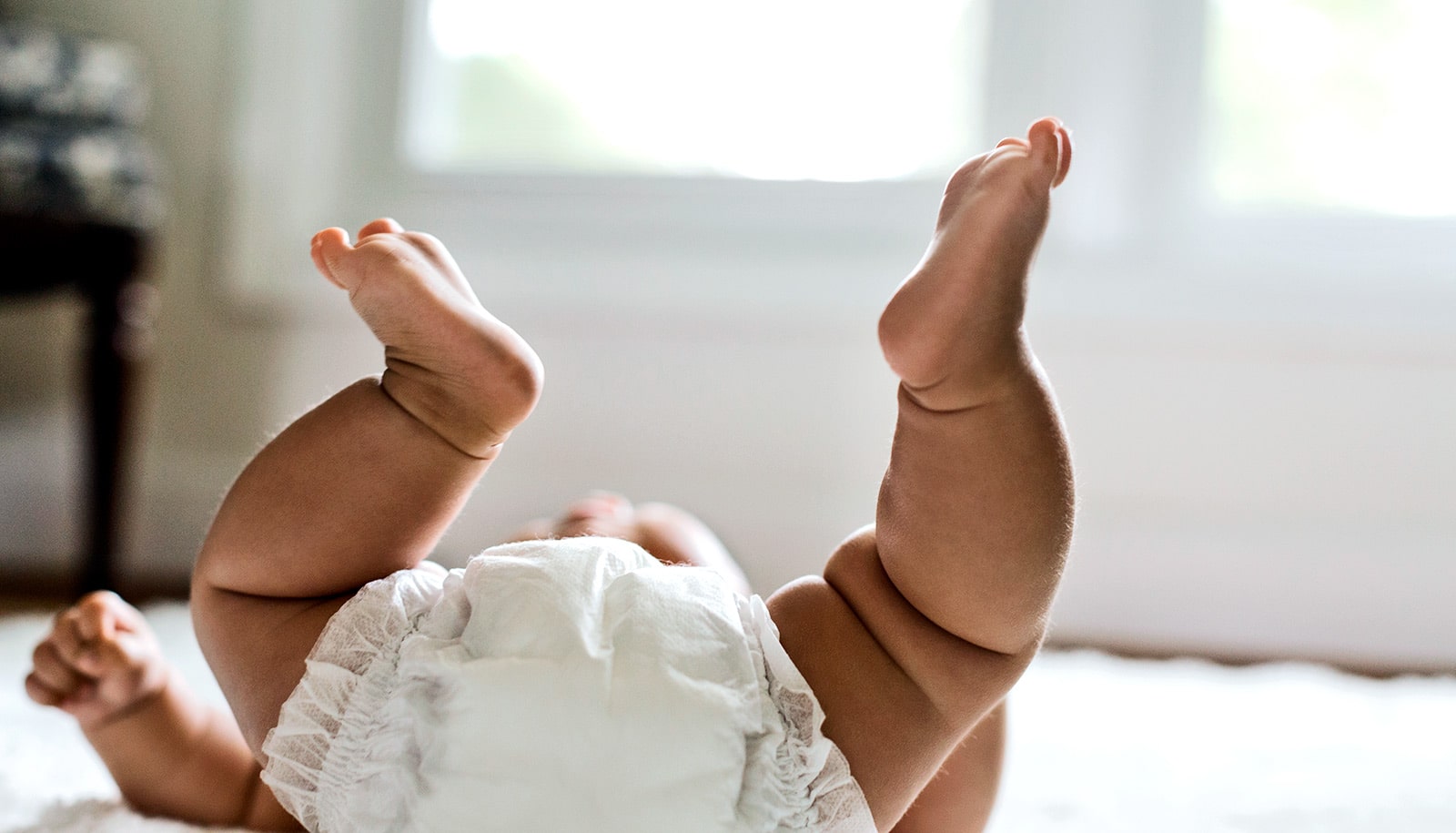 A baby wearing a diaper holds its legs in the air.