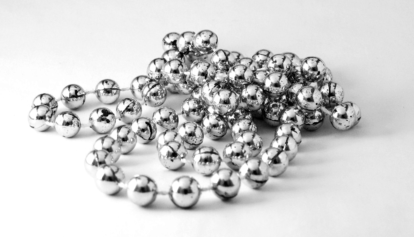A necklace of silver-looking beads sits on a white surface.