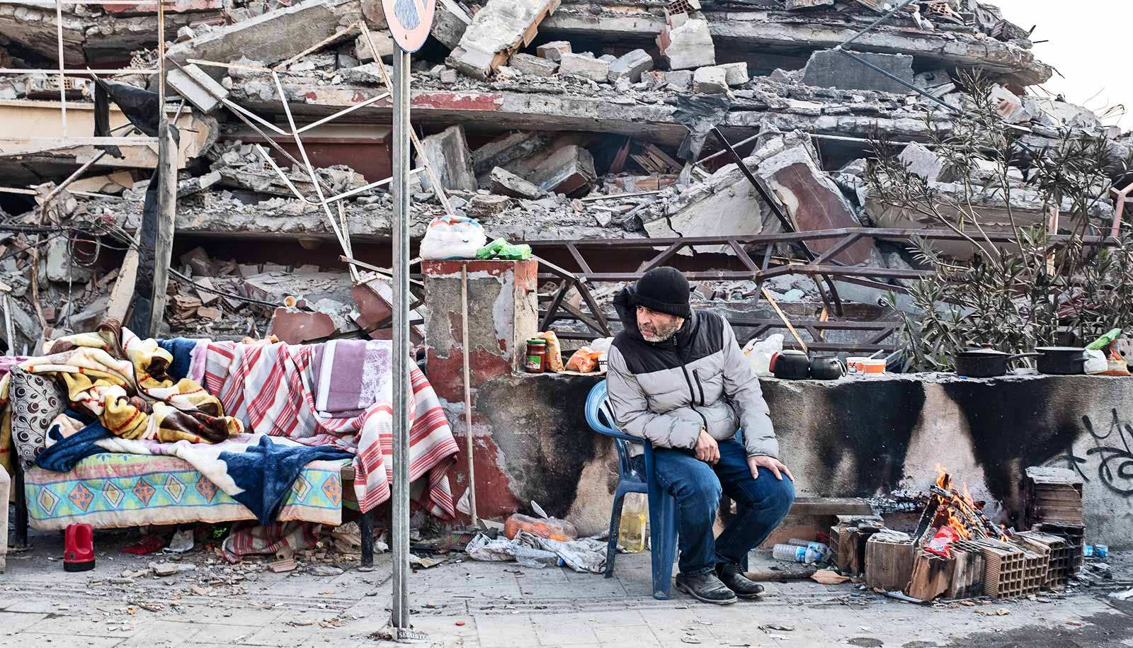A man sits in front of a collapsed building.