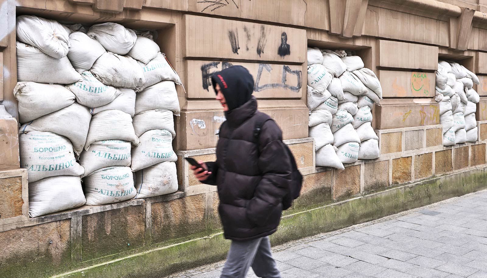 A young man walks past three windows filled up with sandbags.