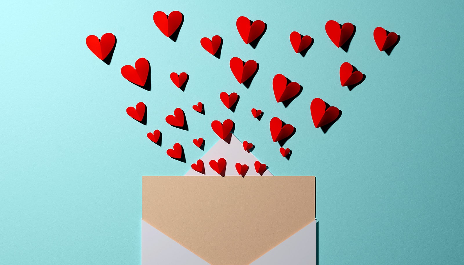 An envelope with a card inside has paper hearts shooting out of it.