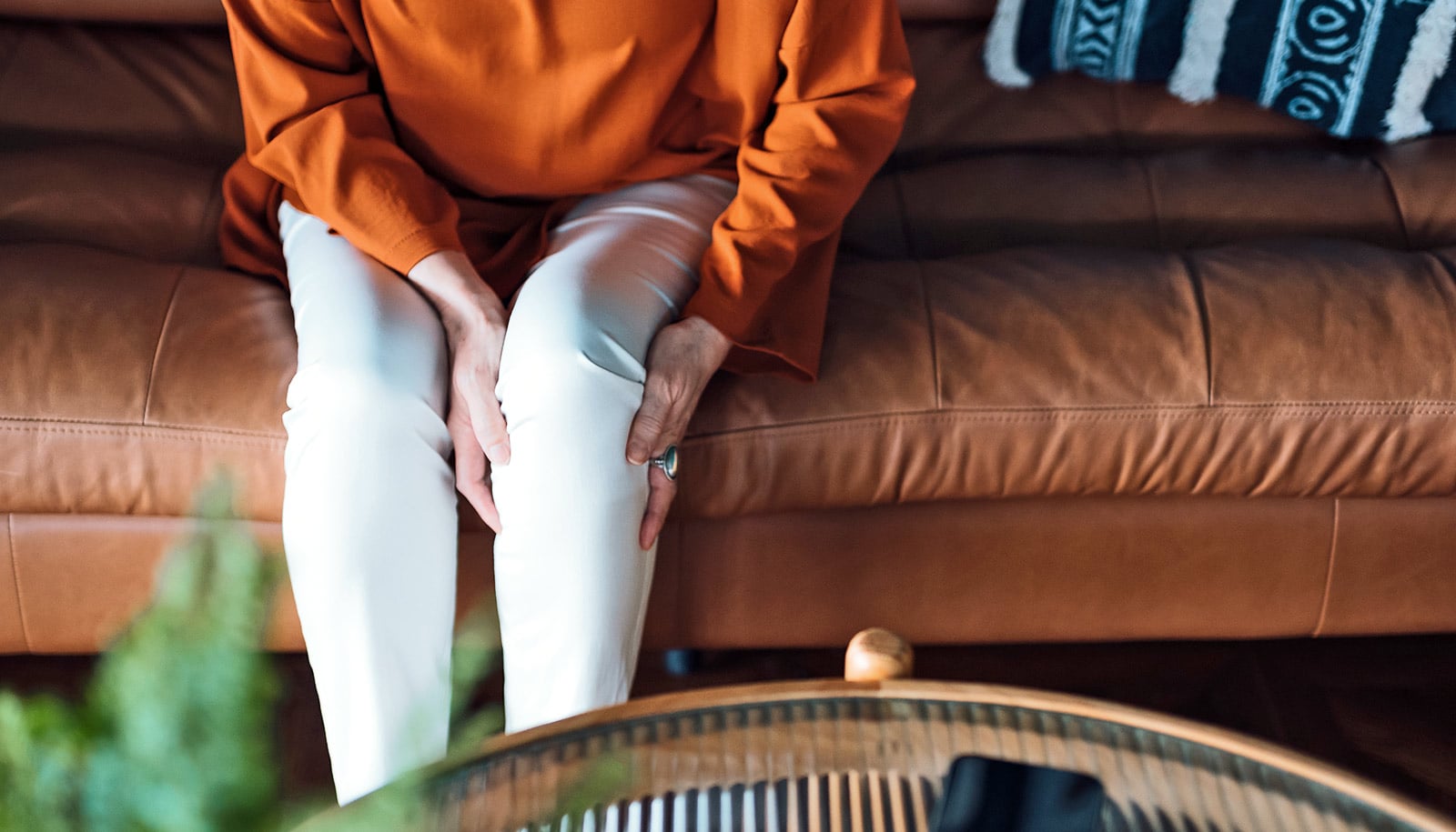 A person sitting on a couch holds their knee in pain.