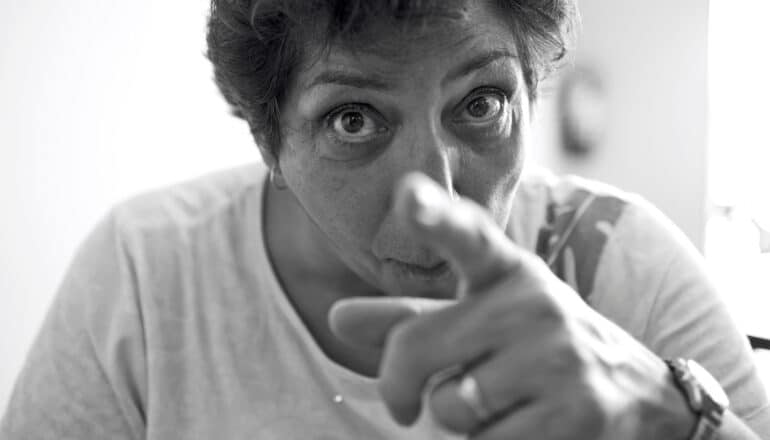 A woman looks angry and points towards the camera.