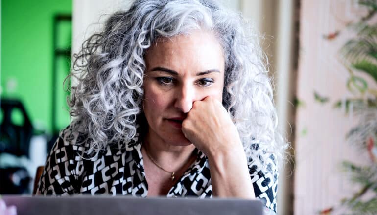 A woman reads her laptop while resting her face on her fist.