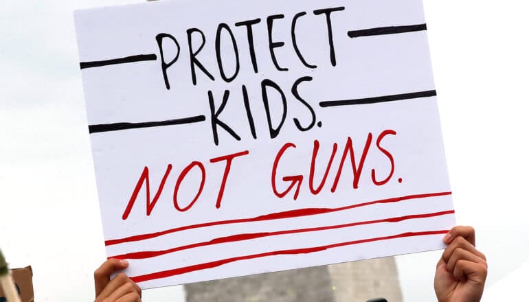 A person holds a sign that reads "Protect kids, not guns."