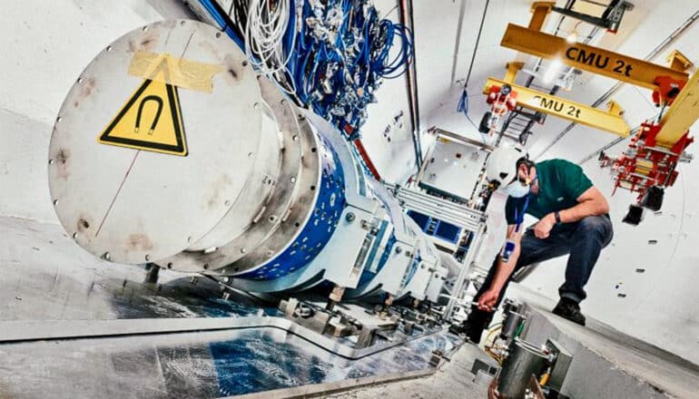 A researcher wearing a hard hat works next to equipment in a long hallway.