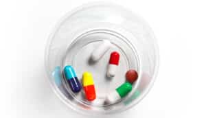 A small plastic cup with several different pills at the bottom on a white background.