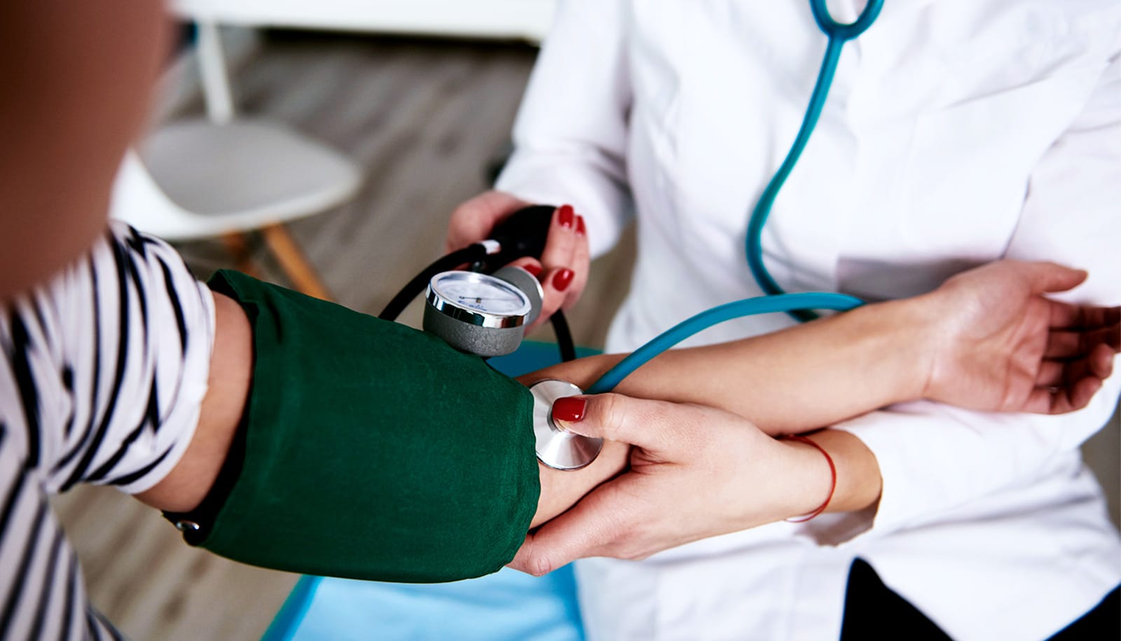 A doctor checks a woman's blood pressure using a cuff and stethoscope.