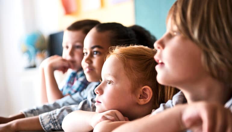 A row of young kids sitting at a classroom table.