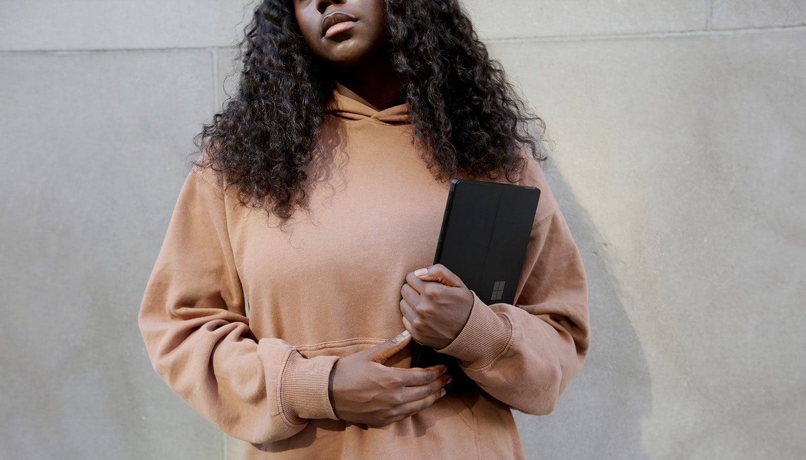 A dark-skinned person in a long, baggy hoodie, carrying a tablet computer