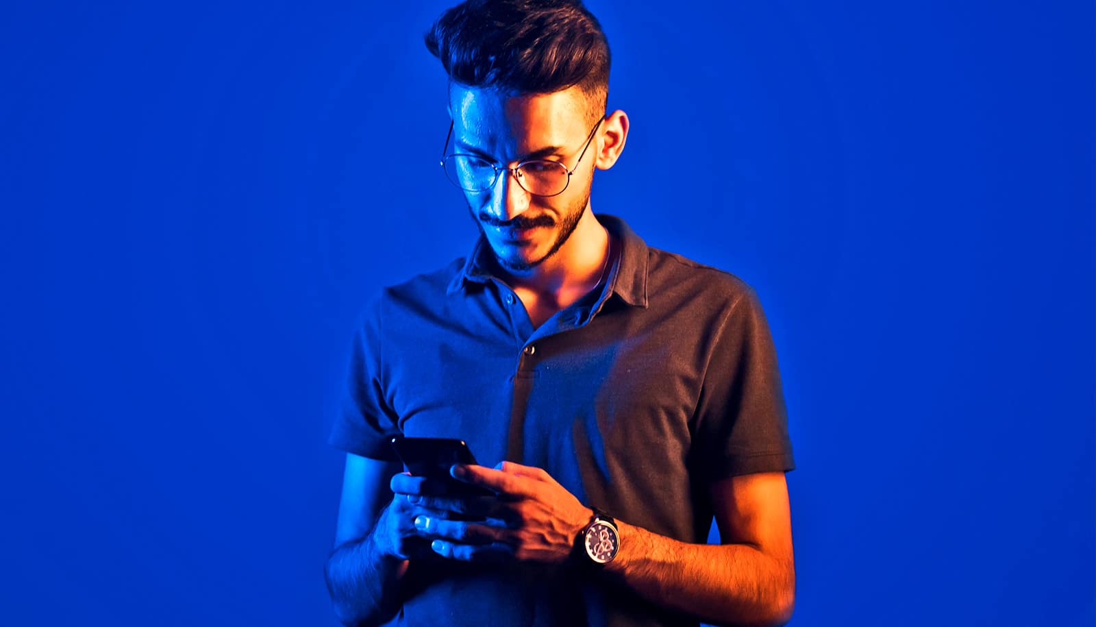 A man reads his phone while blue and orange light illuminate each half of his body.