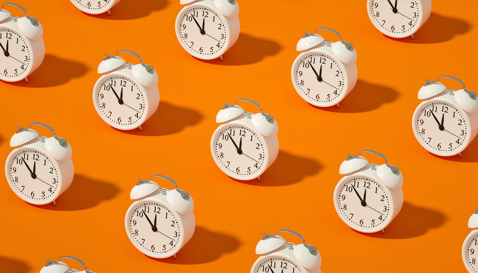 White alarm clocks in rows on an orange background.