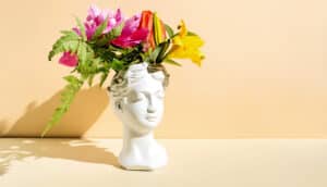 A white human-head shaped vase with brightly colored flowers coming out of the top.