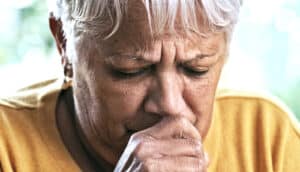 A woman covers her mouth with her hand as she coughs.