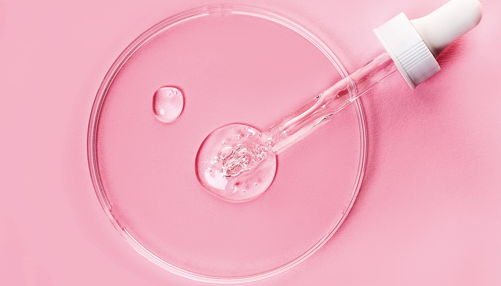 A petri dish with gel from a dropper in it on a pink background.